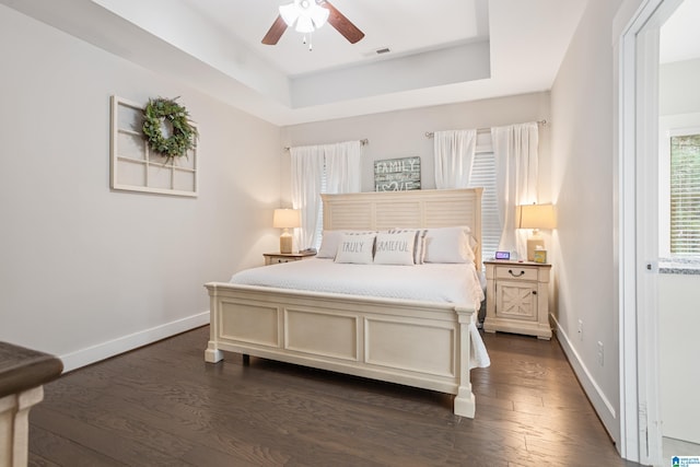 bedroom with dark wood-type flooring, a raised ceiling, and ceiling fan