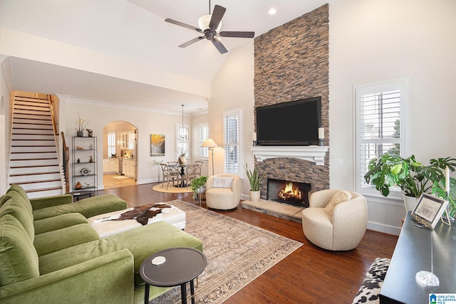 living room featuring a stone fireplace, arched walkways, a wealth of natural light, and wood finished floors