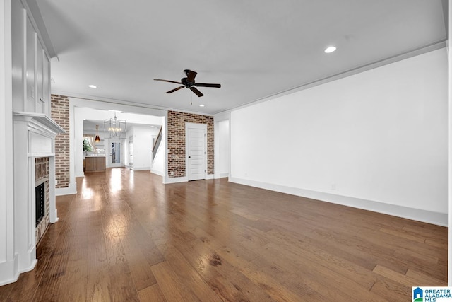 unfurnished living room with hardwood / wood-style floors, crown molding, ceiling fan with notable chandelier, and brick wall