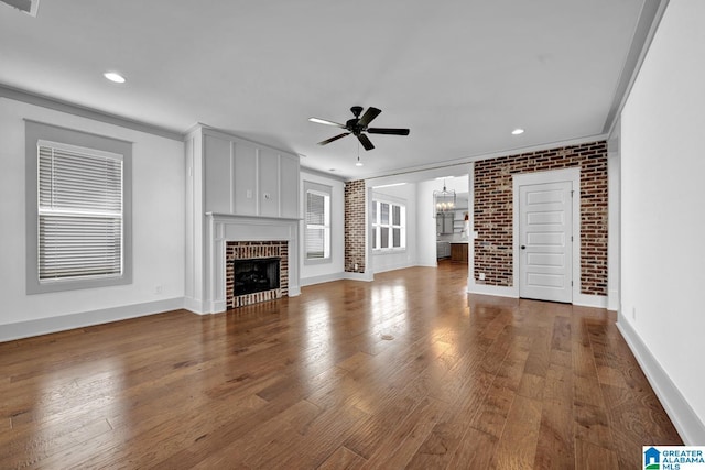 unfurnished living room featuring brick wall, ceiling fan with notable chandelier, hardwood / wood-style floors, a fireplace, and ornamental molding