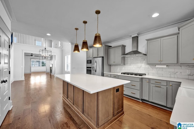 kitchen featuring a kitchen island, appliances with stainless steel finishes, hanging light fixtures, wall chimney range hood, and light hardwood / wood-style flooring