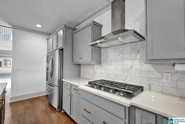 kitchen with appliances with stainless steel finishes, gray cabinetry, backsplash, dark hardwood / wood-style flooring, and wall chimney range hood