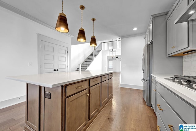 kitchen with wall chimney exhaust hood, tasteful backsplash, a kitchen island, pendant lighting, and stainless steel appliances