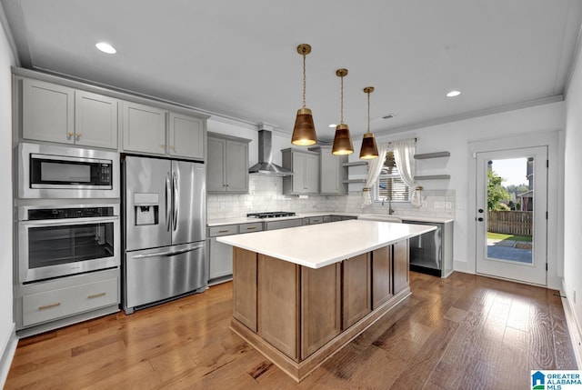 kitchen featuring appliances with stainless steel finishes, pendant lighting, a center island, crown molding, and wall chimney range hood