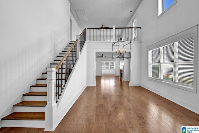 stairway with ceiling fan with notable chandelier, a healthy amount of sunlight, and hardwood / wood-style floors