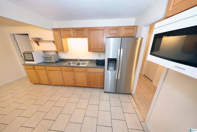 kitchen featuring stainless steel refrigerator with ice dispenser, sink, a textured ceiling, and light tile patterned floors