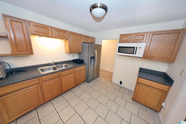 kitchen featuring sink, stainless steel fridge, a textured ceiling, and light tile patterned flooring