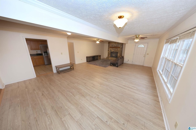 unfurnished living room with a fireplace, ceiling fan, crown molding, a textured ceiling, and light hardwood / wood-style flooring