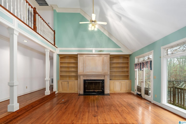 unfurnished living room with high vaulted ceiling, decorative columns, hardwood / wood-style flooring, ceiling fan, and crown molding