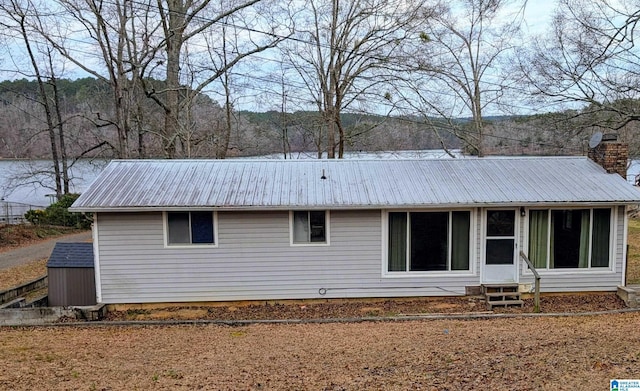 rear view of house featuring entry steps, metal roof, and a chimney