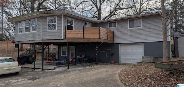 back of property featuring a garage, concrete driveway, stairway, and a wooden deck