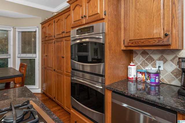 kitchen with crown molding, tasteful backsplash, dark stone counters, stainless steel appliances, and light hardwood / wood-style floors