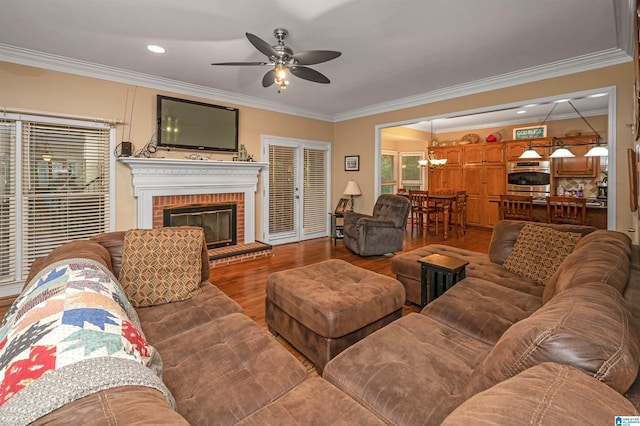 living room with crown molding, ceiling fan with notable chandelier, hardwood / wood-style floors, and a brick fireplace