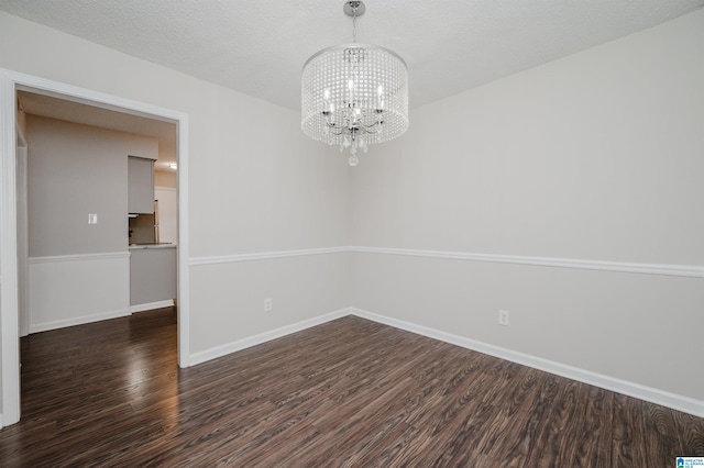 spare room with a textured ceiling, dark hardwood / wood-style floors, and a chandelier