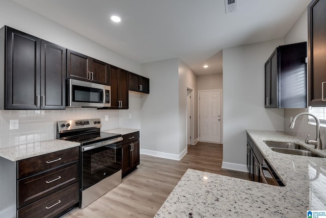 kitchen featuring appliances with stainless steel finishes, tasteful backsplash, sink, light stone counters, and light hardwood / wood-style floors