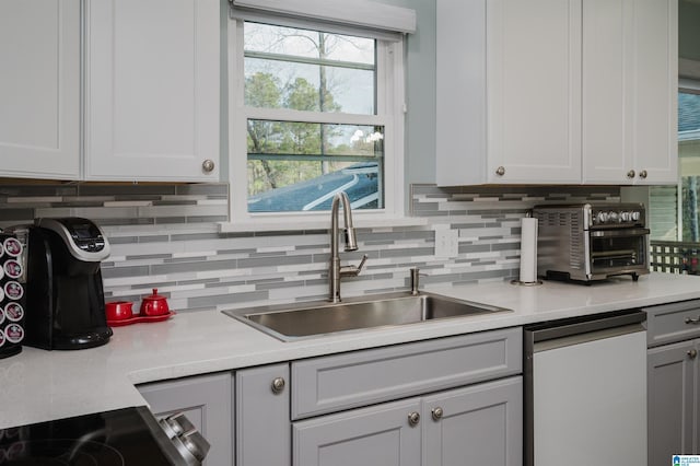 kitchen with white cabinets, tasteful backsplash, sink, and dishwashing machine