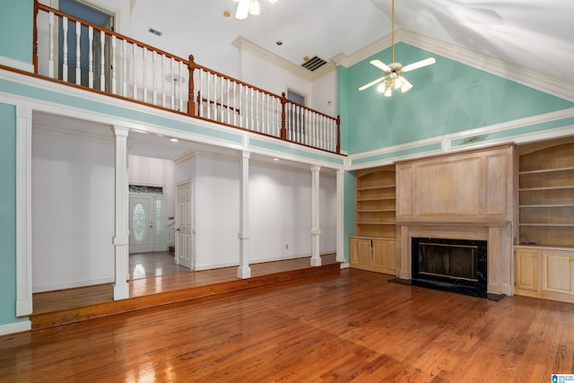 unfurnished living room with crown molding, a premium fireplace, wood-type flooring, built in shelves, and ornate columns