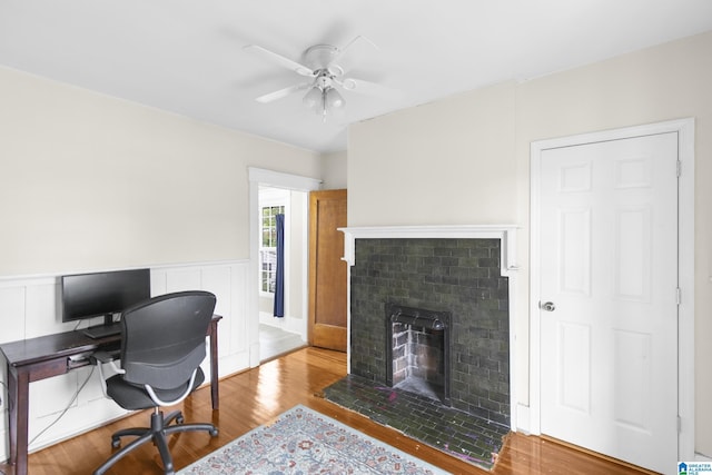 office area with a brick fireplace, light hardwood / wood-style floors, and ceiling fan