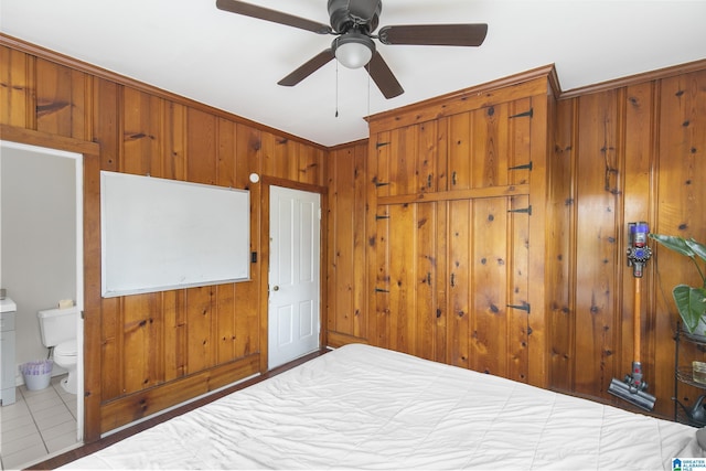 tiled bedroom with connected bathroom, ceiling fan, and wood walls