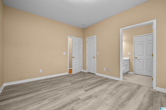 unfurnished bedroom with ensuite bathroom and light wood-type flooring