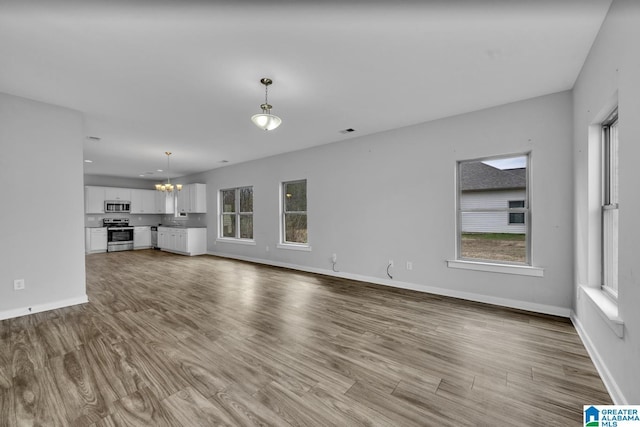 unfurnished living room featuring a healthy amount of sunlight, light wood-type flooring, and a notable chandelier