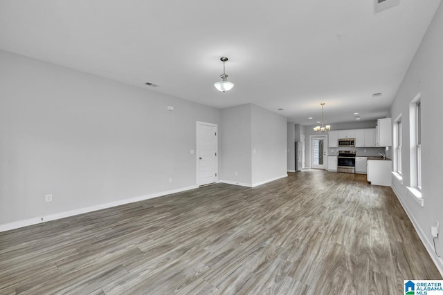 unfurnished living room with an inviting chandelier and light hardwood / wood-style flooring