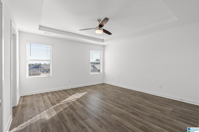 unfurnished room featuring dark hardwood / wood-style flooring, a tray ceiling, and ceiling fan