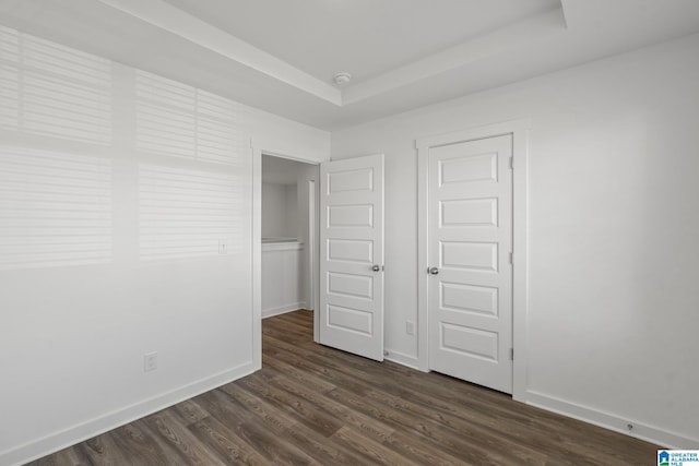 unfurnished bedroom featuring dark wood-type flooring and a tray ceiling