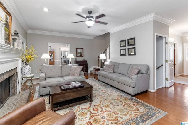 living room with a brick fireplace, hardwood / wood-style flooring, ornamental molding, and ceiling fan