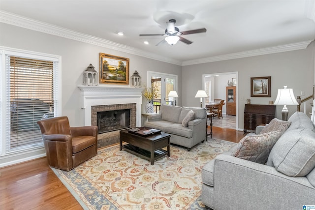 living room featuring crown molding, a brick fireplace, ceiling fan, and light hardwood / wood-style flooring