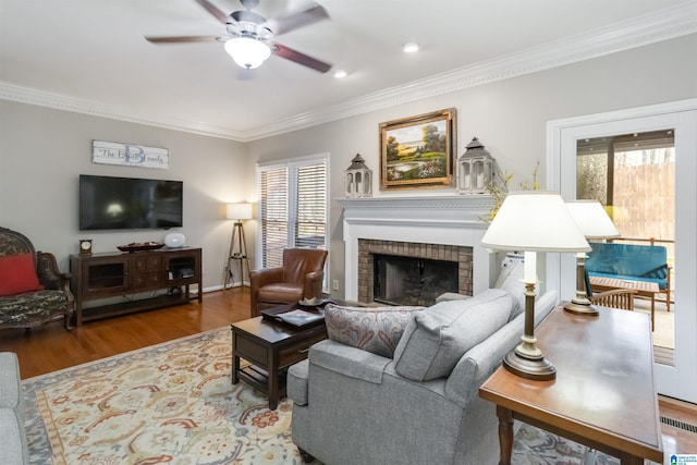 living room with hardwood / wood-style floors, crown molding, a fireplace, and ceiling fan