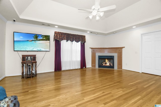 unfurnished living room featuring a tray ceiling, wood-type flooring, ornamental molding, and ceiling fan