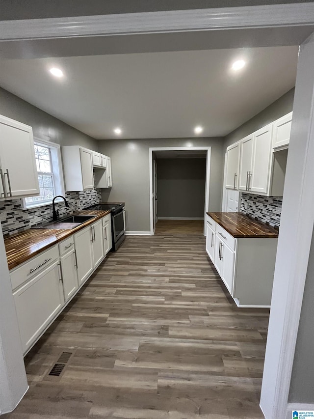 kitchen with sink, butcher block counters, white cabinets, dark wood-type flooring, and stainless steel electric range