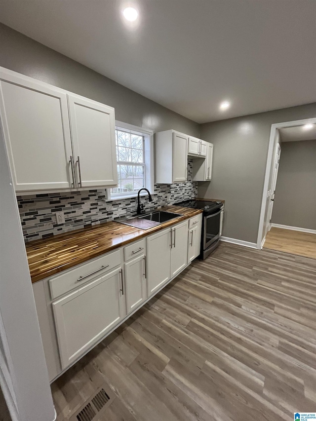 kitchen with sink, wooden counters, stainless steel range with electric stovetop, white cabinetry, and tasteful backsplash