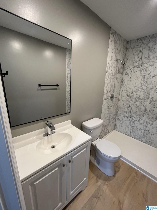 bathroom with vanity, hardwood / wood-style floors, toilet, and tiled shower