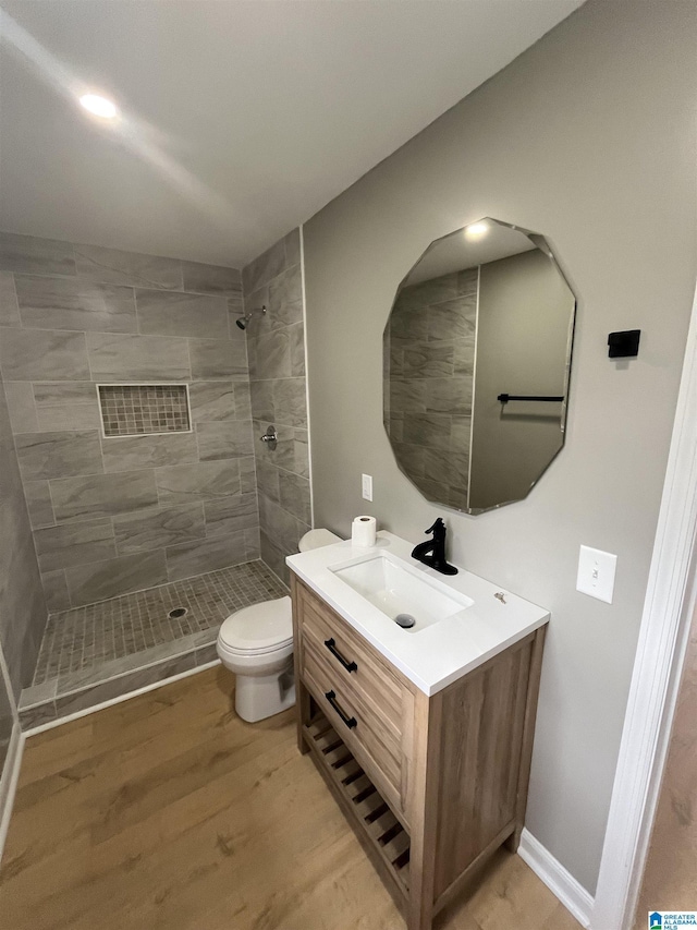 bathroom featuring vanity, hardwood / wood-style flooring, toilet, and a tile shower