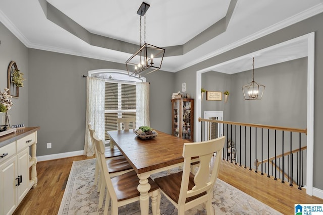 dining area featuring an inviting chandelier, a tray ceiling, light hardwood / wood-style floors, and crown molding