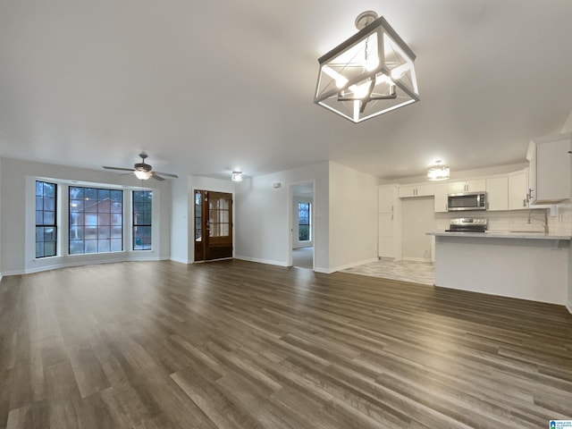 unfurnished living room with sink, ceiling fan with notable chandelier, and dark hardwood / wood-style flooring