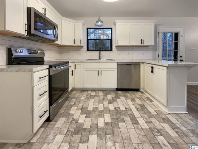 kitchen featuring appliances with stainless steel finishes, decorative light fixtures, sink, white cabinets, and kitchen peninsula