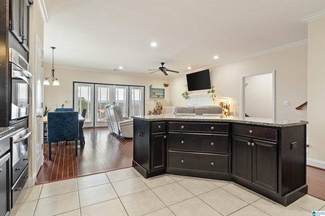 kitchen with pendant lighting, stainless steel oven, crown molding, light stone countertops, and dark brown cabinets