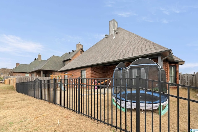 back of house with a trampoline and a lawn