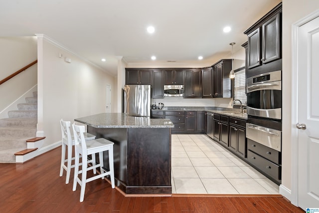 kitchen with hanging light fixtures, stainless steel appliances, a center island, light hardwood / wood-style floors, and dark stone counters