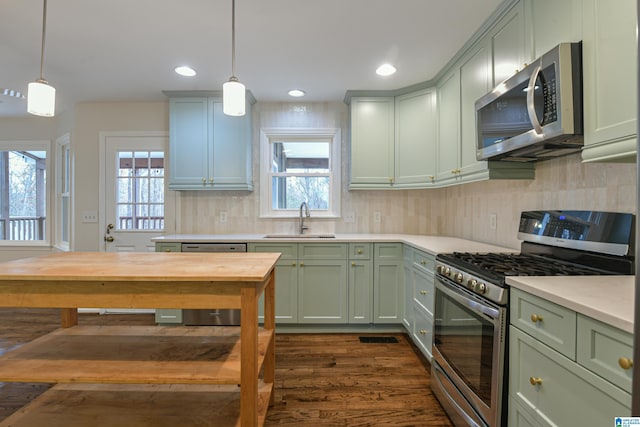 kitchen with dark wood-type flooring, sink, decorative light fixtures, stainless steel appliances, and backsplash