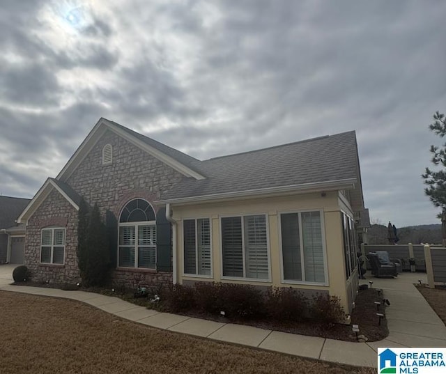 view of front of home with driveway, stone siding, and roof with shingles