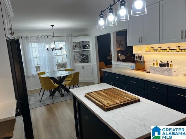 kitchen with light hardwood / wood-style flooring, decorative light fixtures, a center island, ornamental molding, and white cabinetry