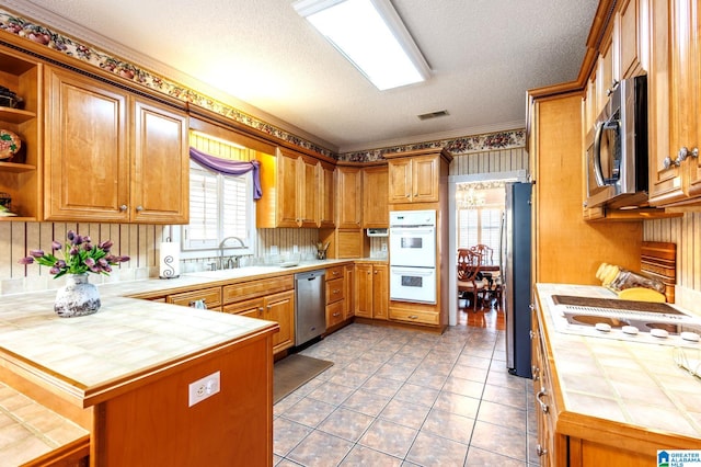 kitchen with sink, a textured ceiling, tile counters, kitchen peninsula, and stainless steel appliances