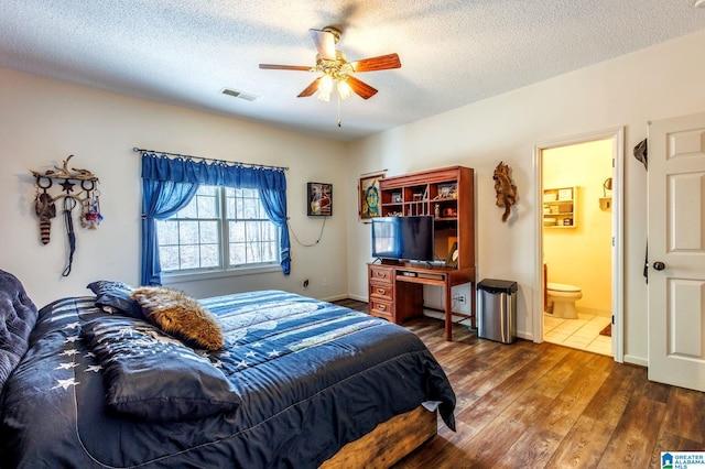 bedroom with ceiling fan, dark hardwood / wood-style floors, a textured ceiling, and ensuite bath