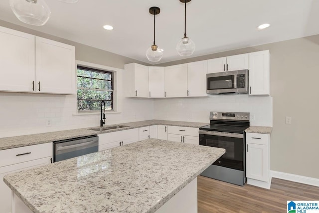 kitchen featuring light stone counters, decorative light fixtures, stainless steel appliances, white cabinets, and a sink