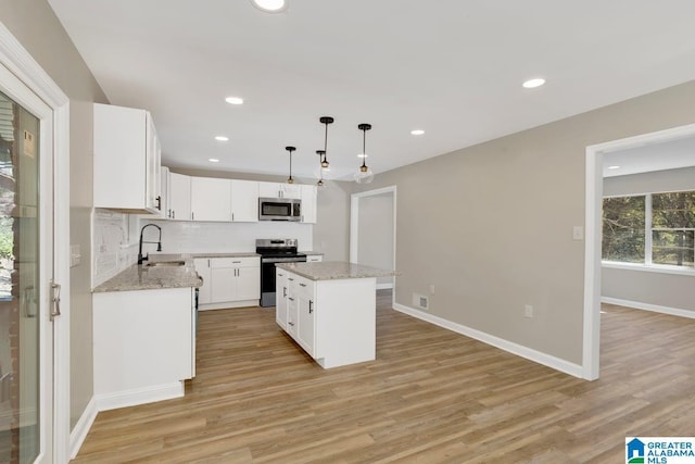 kitchen featuring a kitchen island, appliances with stainless steel finishes, white cabinetry, pendant lighting, and a sink