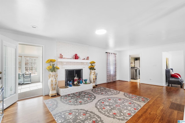 living room with hardwood / wood-style flooring, crown molding, and a brick fireplace